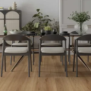 Modern dining area in a bright kitchen: six dark chairs around a long wooden table, with plants, a glass vase, white cabinetry, and built-in ovens in the background.