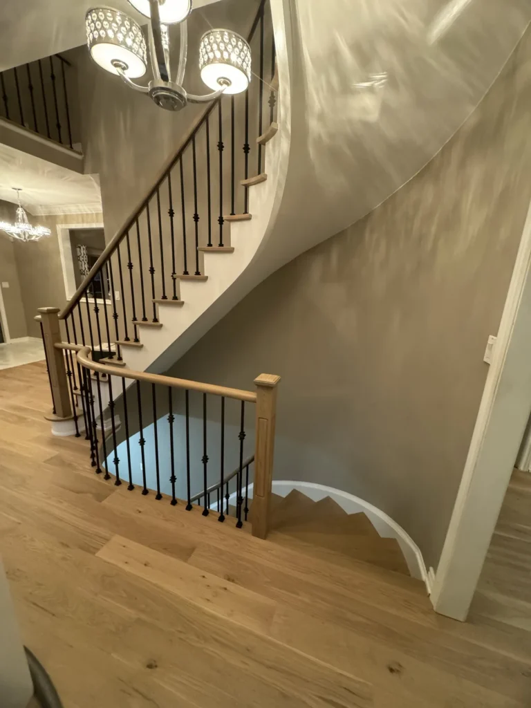 White oak staircase with black wrought iron spindles curving up from the hallway of a Bolton home
