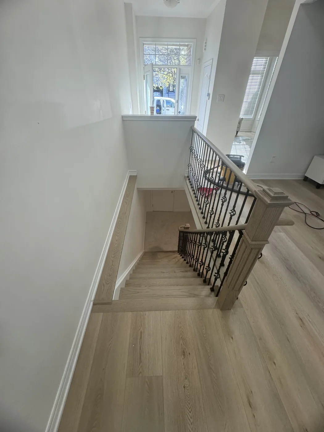 Straight staircase in Richmond Hill going down to the lower level, light treads, grey-toned newel posts and handrail, decorative black iron spindles