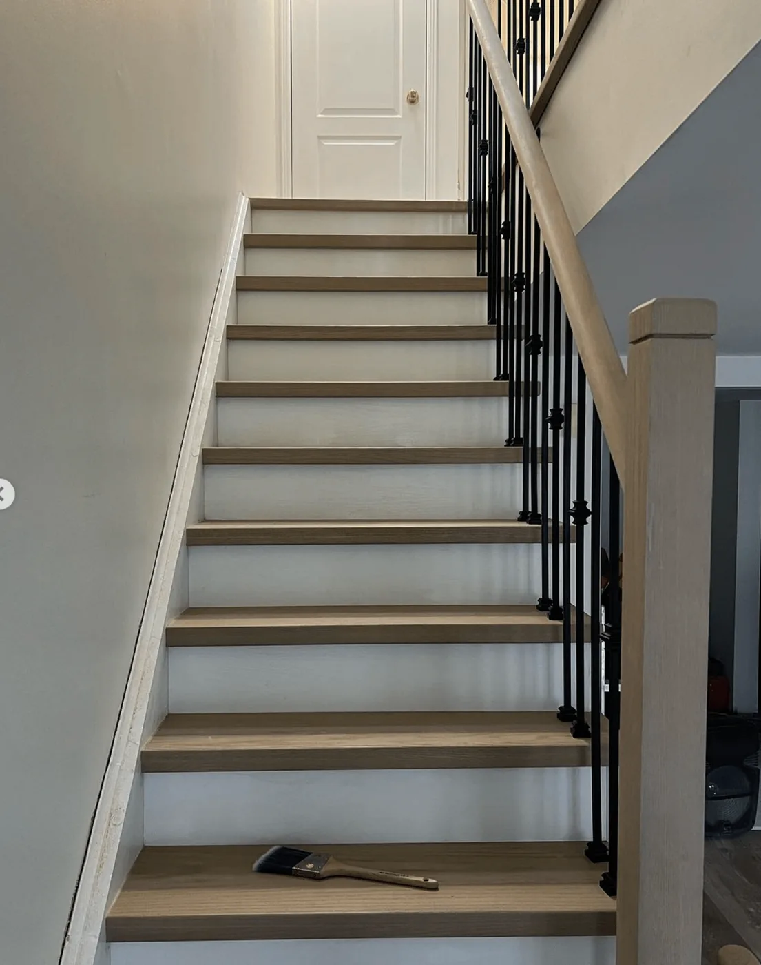 Greige (grey-brown) stair treads with white risers, a grey-beige newel post and black iron spindles, Toronto