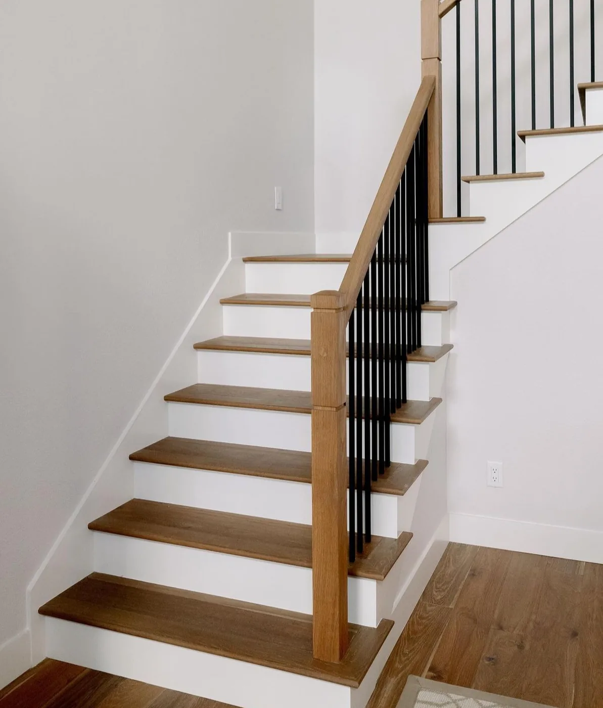 Warm honey-brown oak stair treads with white risers, a light oak handrail and black iron spindles, matching the hardwood floor, Whitby