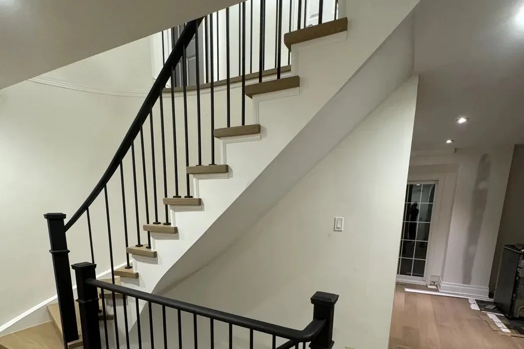Curved staircase in Richmond Hill with light oak treads and risers, black newel posts, black handrail and black iron spindles