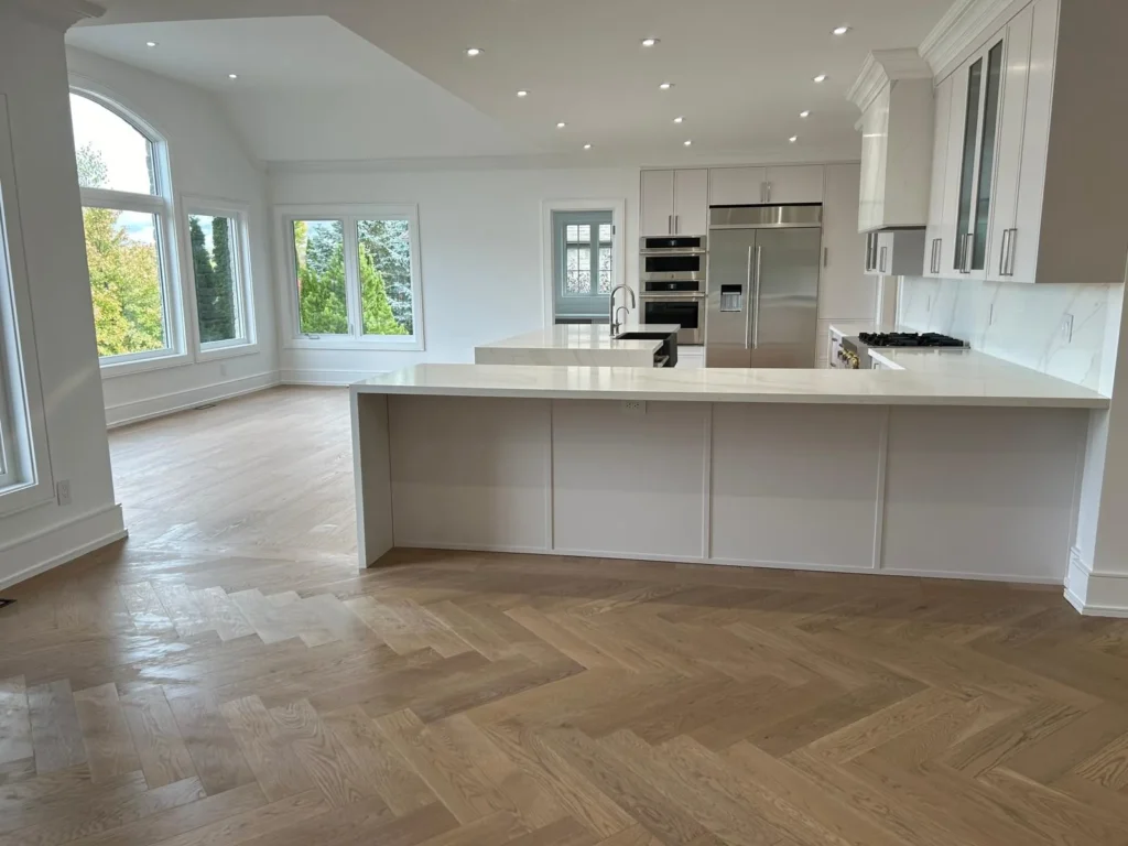 White oak herringbone floor in a white Toronto kitchen, meeting straight planks in the breakfast area