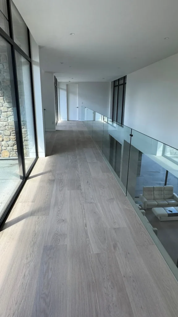 Wide plank white oak hardwood along an upstairs hallway with a glass railing in a Toronto home